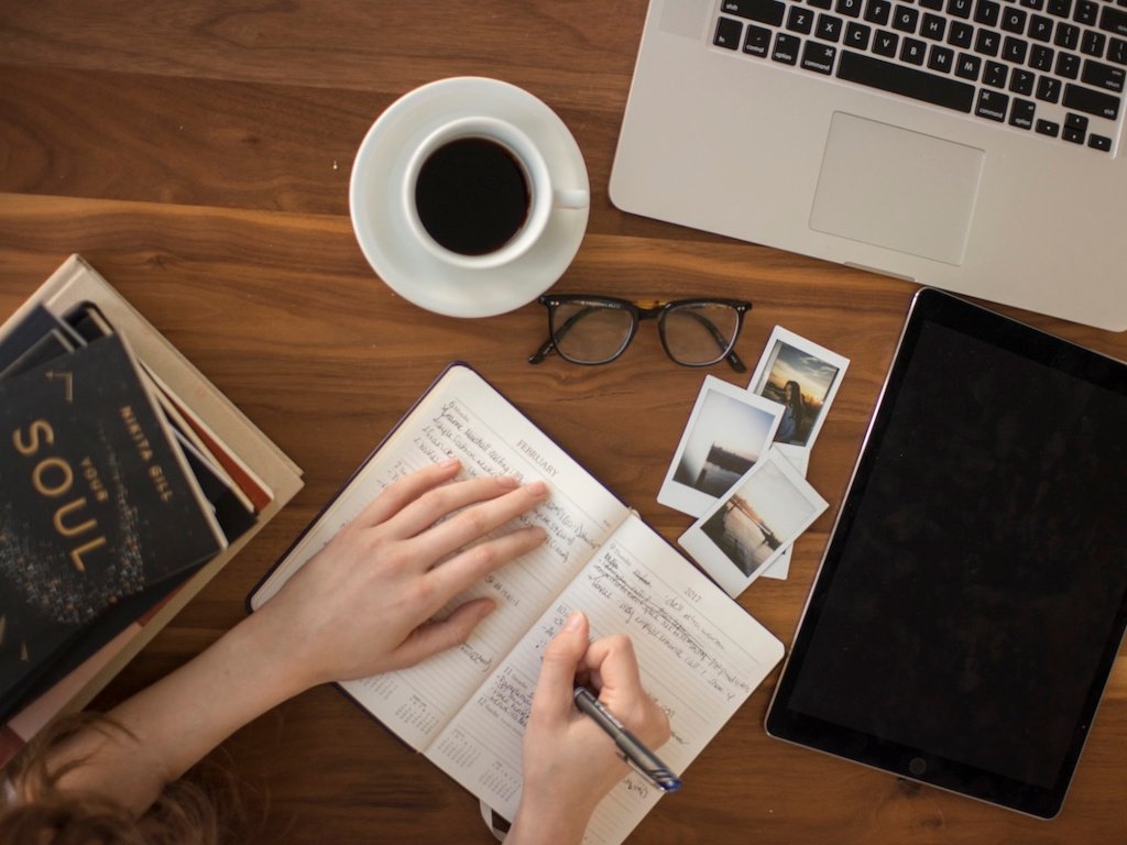 A planner with a coffee cup and pen on a wooden desk.
